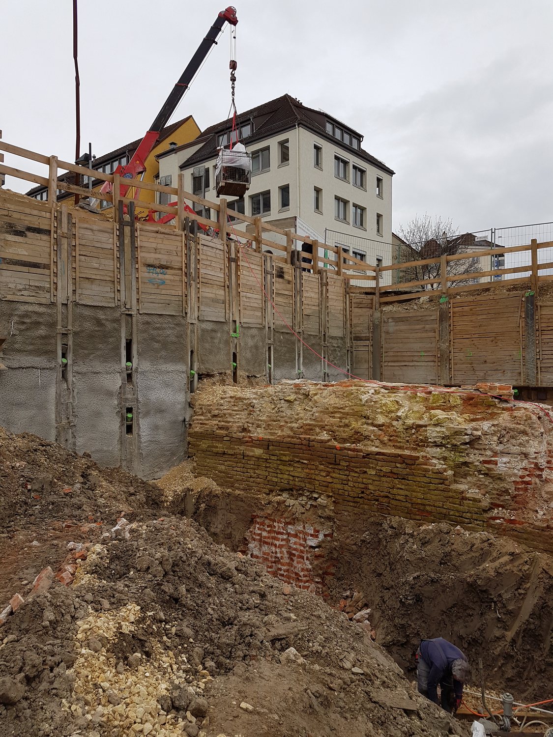 Kran hebt Material in die tiefe Baugrube, Ulmer Stadtbebauung im Hintergrund